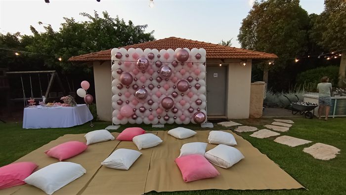 קיר בלונים ורוד וכריות על הדשא